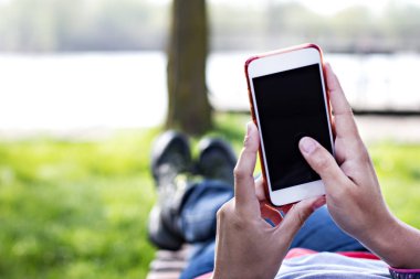 Bir şezlong nehrin arka planı kadının elinde cep telefonu. Telefon, şezlong, Yeşil çimenler, nehir. Dinlenme zamanı. Tatil, doğada telefon üzerinde çalışmak.