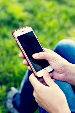 Bir şezlong arka planı yeşil çim kadının elinde cep telefonu. Dinlenme zamanı. İş dinlenme tatile bir akıllı telefon kullanan kadın, yalan ayakları kızlar, açık havada, park, yaz