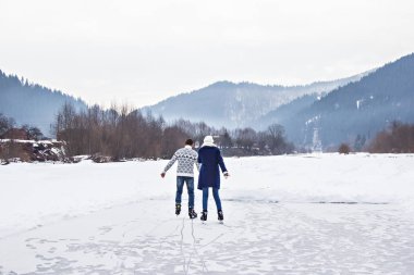 Sıcak kazaklı, sevgi dolu bir çift donmuş bir gölde paten kayıyor.
