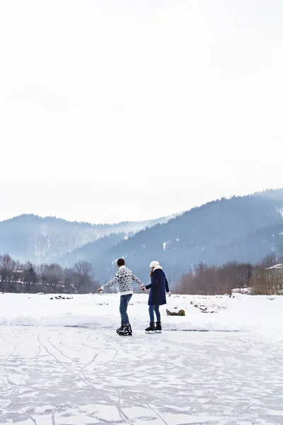Liebespaar in warmen Pullovern auf Schlittschuhen auf einem zugefrorenen See — Stockfoto