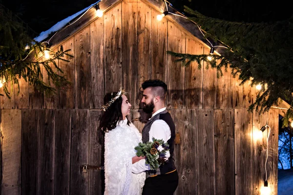 Pareja recién casada, novia y novio en el fondo de una antigua casa de madera y guirnalda retro . —  Fotos de Stock