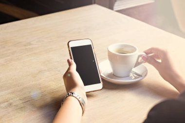 girl drinks espresso in a cafe and looks at a  phone