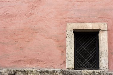 Parmaklıklı pencereli eski pembe bir duvar. Kapalı bir depo penceresi, buzlu cam ve bir ızgara, taş çerçeve. Parçalanmış eski pembe duvar