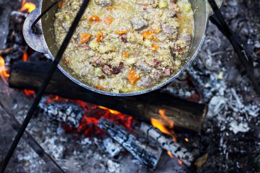 Yulaf lapası ve etli şenlik ateşi. Arkasında dağlar olan geleneksel bir kazanın altında yangın. Yaz kampı kavramı. 