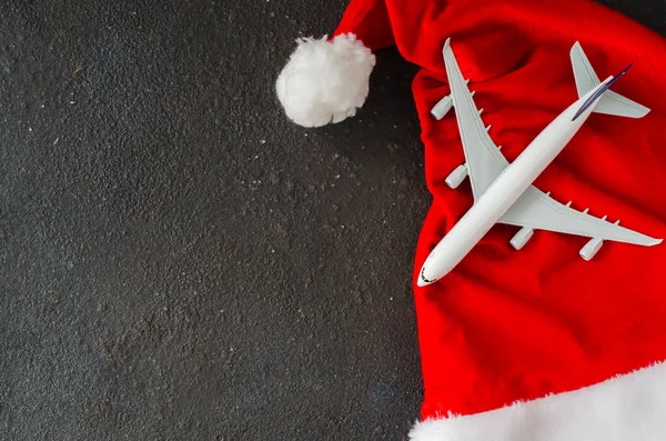 Seyahatler ya da Noel seyahati planları. Oyuncak uçak ve Noel Baba şapkası koyu betonda..