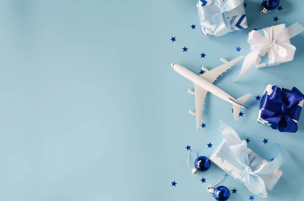 Noel ya da yeni yıl seyahati konsepti. Pasaportlu oyuncak uçak ve mavi arka planda hediye kutuları..