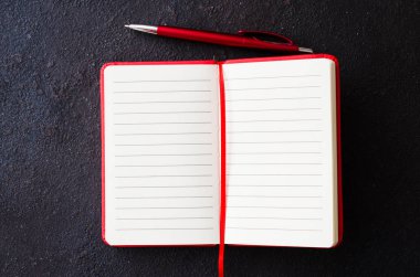 Koyu arka planda kırmızı kalemle boş kırmızı defter. Metin için boş kağıt.
