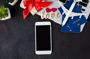 Seyahat rezervasyonu konsepti. Akıllı telefon, uçak modeli, dizüstü bilgisayar, pasaport ve karanlık arka planda hediye kutusu..