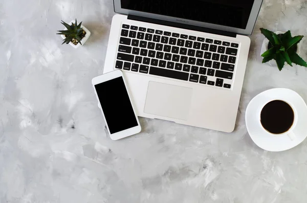 White smartphone with black blank screen on office desk with laptop and cup of coffee. Mock up of phone.