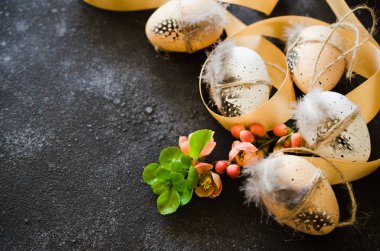 Süslü Paskalya arkaplanı. Süslü paskalya yumurtaları. Tüyleri, kurdelesi ve çiçekli bahar dalıyla. Koyu beton arka planda..