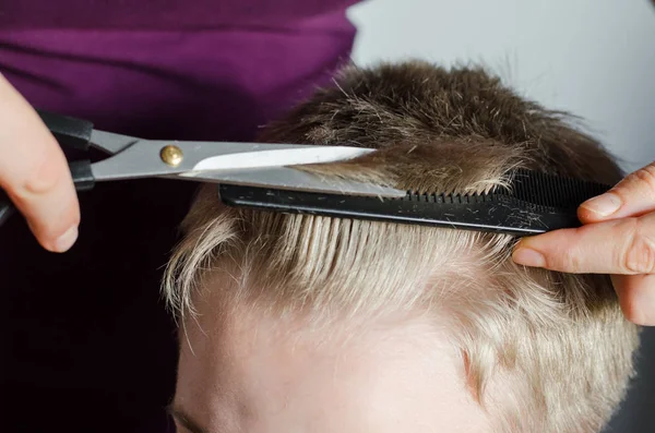 Woman cuts hair of boy at home. Homemade haircut by scissors for hair