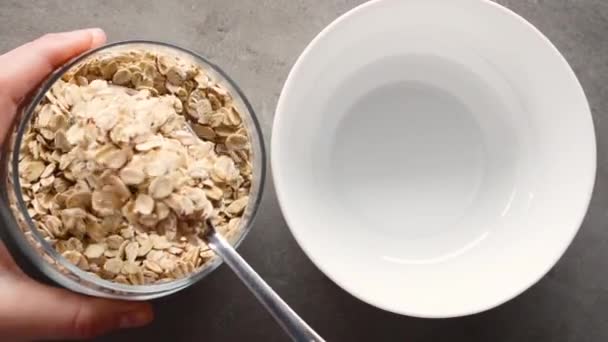 Woman pours dry oatmeal into empty white bowl. — Stock Video
