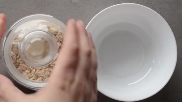 Woman pours dry oatmeal into empty white bowl. — Stock Video