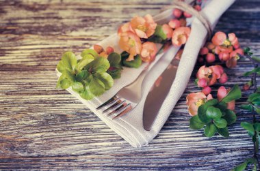 Rustik eskipli masada keten peçete üzerinde narin çiçeklerle vintage masa ayarı, yakın çekim. Çiçek dekoruna sahip Tatil Masa Seti