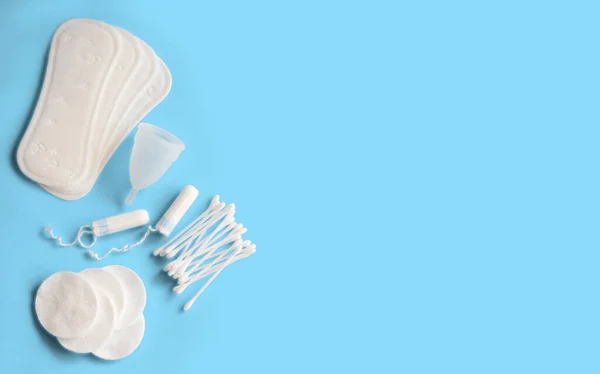 Feminine hygiene accessories. Concept of feminine hygiene during menstruation. Sanitary pad, menstrual cup and tampons, cotton buds and cotton pads on blue background. Flat lay, top view