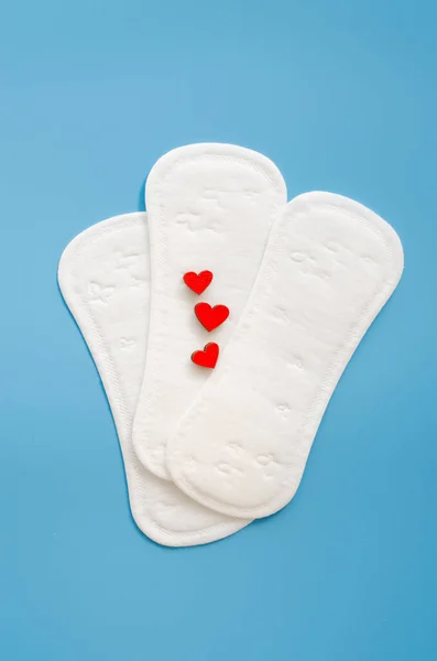 Feminine hygiene pad with red heards on blue background. Imitation of bleeding. Concept of feminine hygiene during menstruation. Flat lay, top view