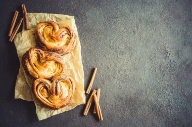 Fırında taze kokulu tarçınlı çörekler. Koyu arka planda geleneksel ev yapımı hamur işleri. Rustik stil.
