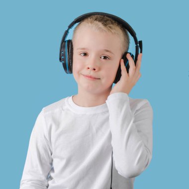 Küçük çocuk ellerini kulaklığın üzerine koy ve müzik dinle. Kulaklıklı çocuk kameraya bakıyor.