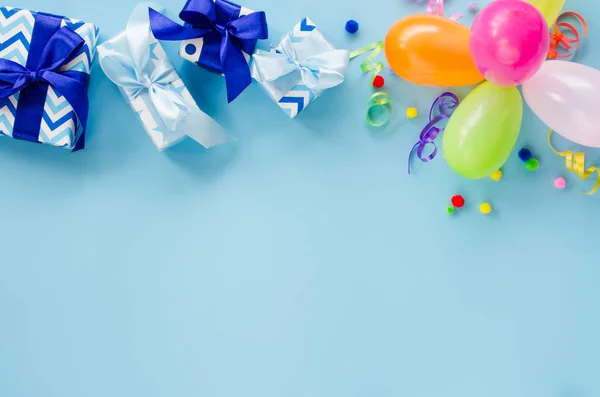 Party or birthday blue background. Holiday mockup. Greeting card with copy space. Frame with colorful balloon, gift boxes and serpentine. Top view. Flat lay.
