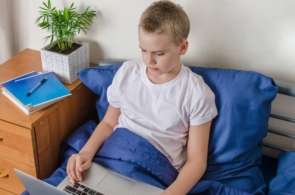 Distance learning and online education concept. Schoolboy studying at home. Boy with laptop lies in bed. Social distance during quarantine.