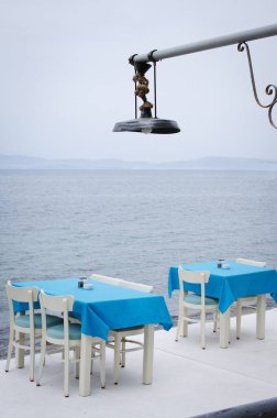 Deniz manzaralı sıcacık bir kafenin terasında hasır masalar ve sandalyeler. Kötü bir gün.
