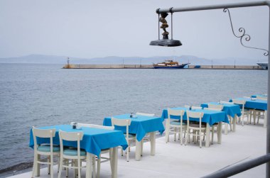Deniz manzaralı sıcacık bir kafenin terasında hasır masalar ve sandalyeler. Kötü bir gün.