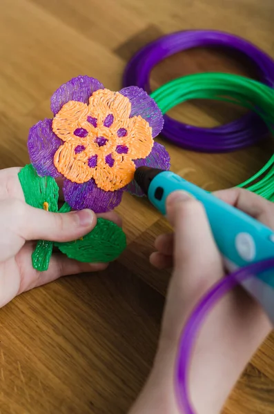 3 boyutlu kalem kullanan bir çocuk. Çocuk elleri renkli ABS plastikten çiçek yapıyor. Evde yaratıcı hobi, teknoloji, eğlence, eğitim konsepti. Seçici odak.