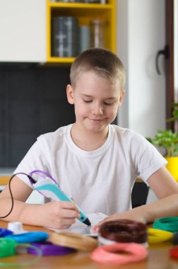 3 boyutlu kalem kullanan bir çocuk. Çocuk evde renkli ABS plastiği ile şablonla resim çiziyor. Evde yaratıcı hobi, teknoloji, eğlence, eğitim konsepti. Seçici odak.