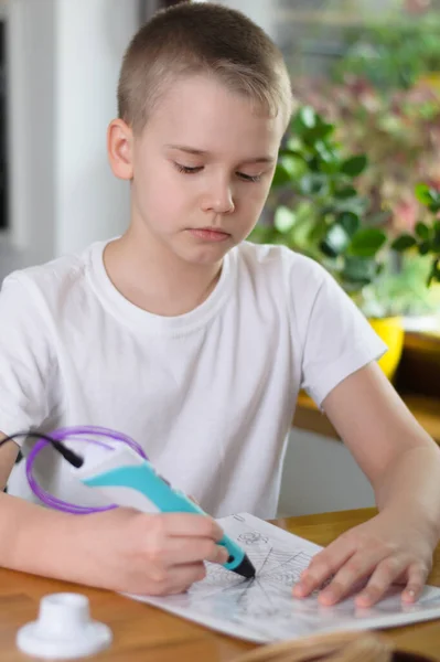 3 boyutlu kalem kullanan bir çocuk. Çocuk evde renkli ABS plastiği ile şablonla resim çiziyor. Evde yaratıcı hobi, teknoloji, eğlence, eğitim konsepti. Seçici odak.