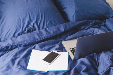 Laptop, akıllı telefon ve defter sabah vakti yatağın üstünde. Yatak odası, ev konsepti..