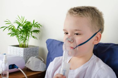 Hasta çocuk astım maskesi ile nefes alıyor. Koronavirüs, astım ve alerji gibi solunum hastalıklarının önlenmesi için nebulizör ve sprey kullanımı. Evde terapi..