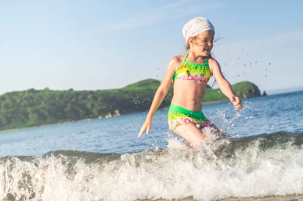 Девушка, бегущая по пляжному берегу брызгает водой в голубом море — стоковое фото