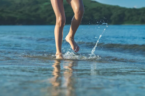 青い海で水しぶきビーチの海岸を走っている少女 — ストック写真