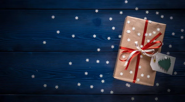 Christmas present with a red ribbon on a blue background with snowflakes — Stock Photo, Image