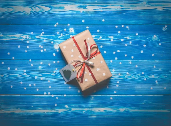 Το Top view χριστουγεννιάτικο δώρο με μια κόκκινη κορδέλα σε μπλε φόντο με νιφάδες χιονιού — Φωτογραφία Αρχείου