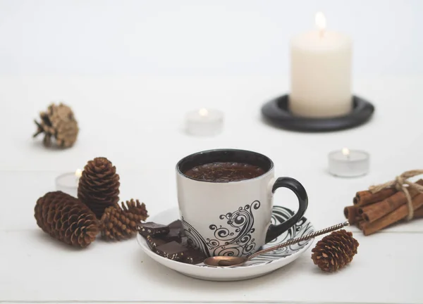 White Cup of hot coffee surrounded by candles, fir cones, cinnamon on white background. — Stock Photo, Image