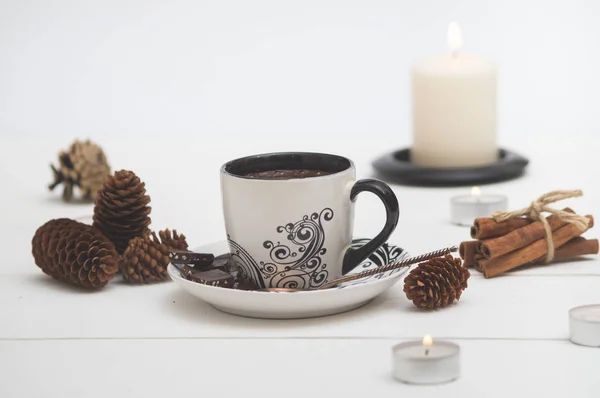 White Cup of hot coffee surrounded by candles, fir cones, cinnamon on white background. — Stock Photo, Image