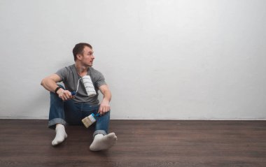 adam duvara oturan ve bir rulo ve fırça ile beyaz duvar boyama işlemine hazırlanıyor