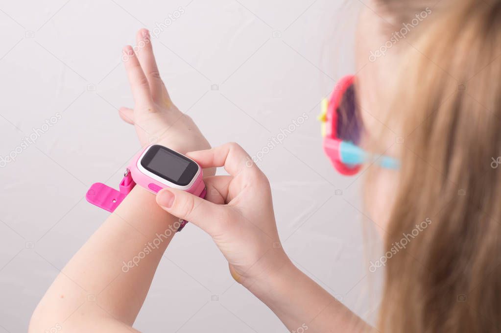 Technology for children: a girl wearing pink glasses uses a smartwatch.
