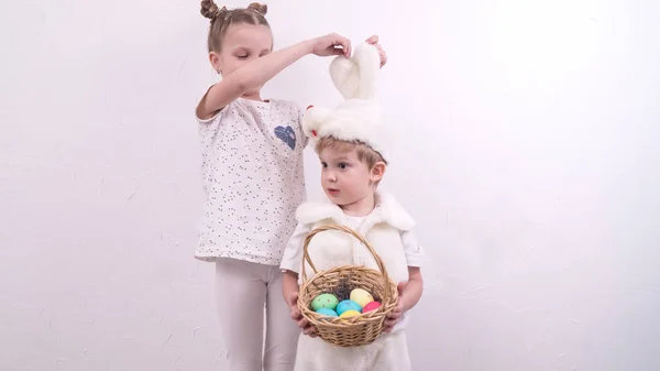 Brother and sister celebrate Easter. The boy is dressed in a rabbit costume and holds a korunzku with Easter eggs. — Stock Photo, Image