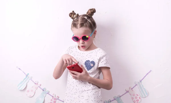 Una chica con gafas rosas usa un smartphone rojo . —  Fotos de Stock