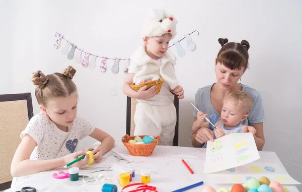 Påskhögtiden: Familjen vid bordet. Mamma visar barnen hur man målar påskägg. — Stockfoto