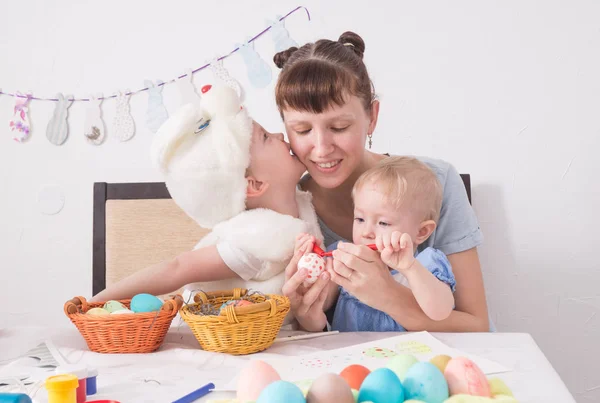 Familjen firar påsk: mamma målar ett mönster på Easter egg. Sonen kysser sin mor på kinden. — Stockfoto
