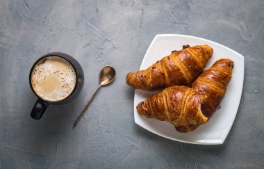 Kahve ve hamur işleri: siyah bir kupa kahve, bir gümüş kaşık ve çörek üzerinde gri bir arka plan üzerine bir daire ile.