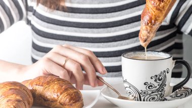 Bir kahve bir kruvasan daldırma bir el görünümünü yakın çekim