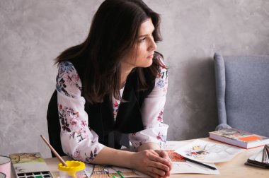 Düşünme: kadın Tasarımcısı onu dirsekler masanın üzerine eğildi ve düşündü. Dikkatsizce dağınık masa skeçler, renkleri, not defteri, malzeme ve renk örnekleri.