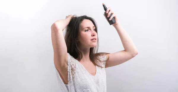 自然派化粧品: 長い髪の女の子は髪をスプレーします。白い背景の上のモデル. — ストック写真