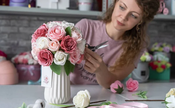 Una chica recoge un ramo de rosas rosadas y blancas en un jarrón blanco . — Foto de Stock