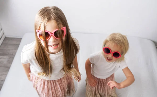 Dos hermanas con gafas de sol rosas y los mismos trajes sobre un fondo blanco . —  Fotos de Stock