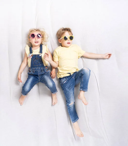 Niño y niña en gafas de sol se acuestan en el sofá y se divierten . —  Fotos de Stock